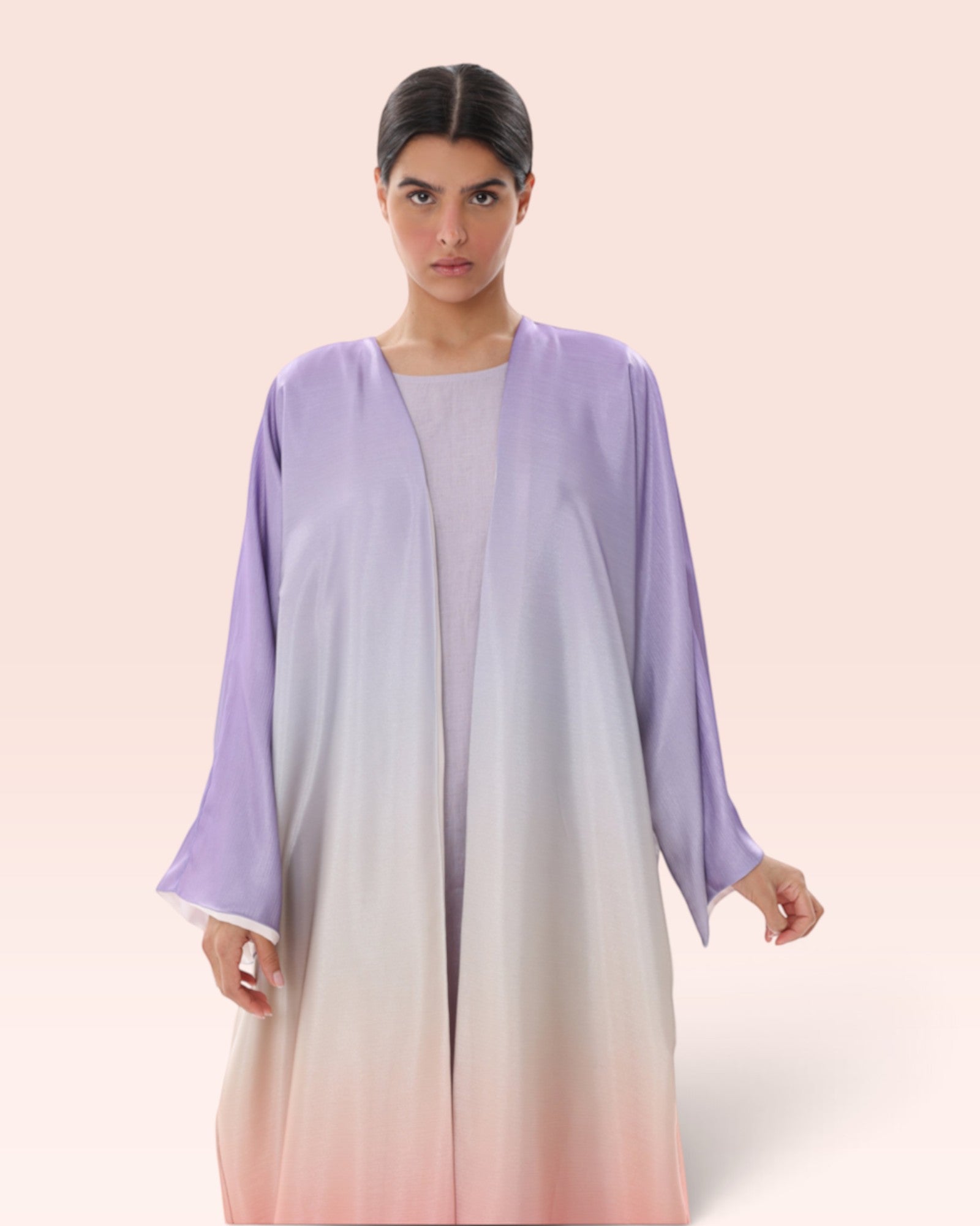 Model wearing an Amore Abaya Boutique Sunset Ombre Bisht Abaya in light purple to peach gradient flowy fabric.