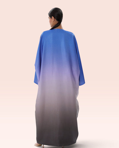 Back view of a woman wearing an Amore Abaya Boutique Sunset Ombre Bisht Abaya in blue to grey gradient fabric.